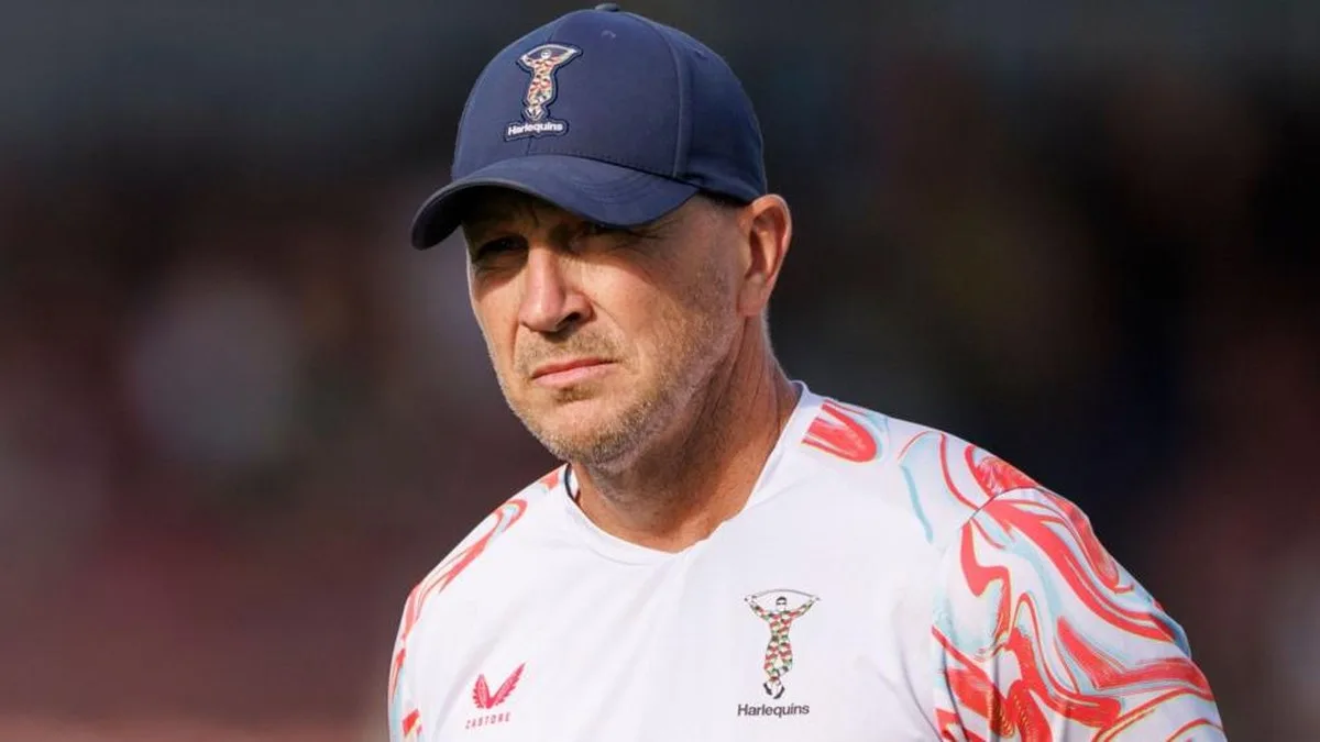Jason Gilmore wearing a navy blue Harlequins baseball cap and a white Harlequins training top with red and light blue patterns on the shoulders and sleeves