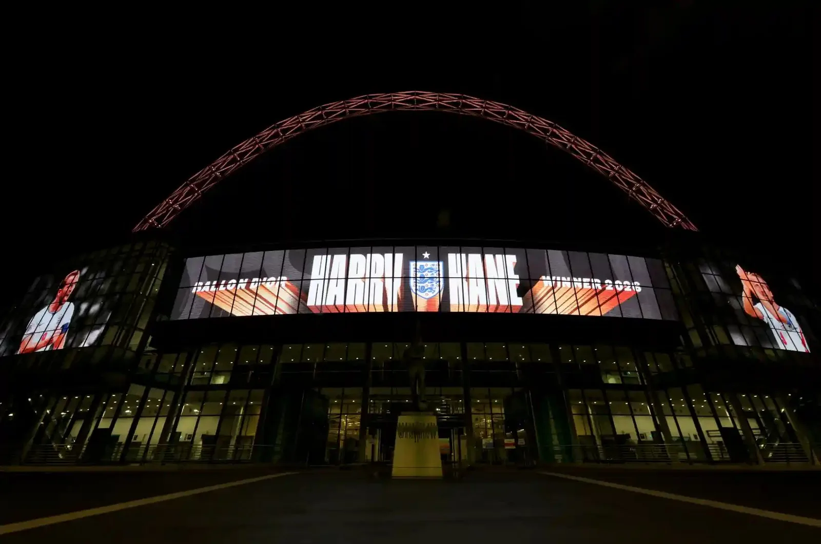 Wembley Stadium's arch lit up at night, with a screen celebrating Harry Kane's Ballon d'Or win