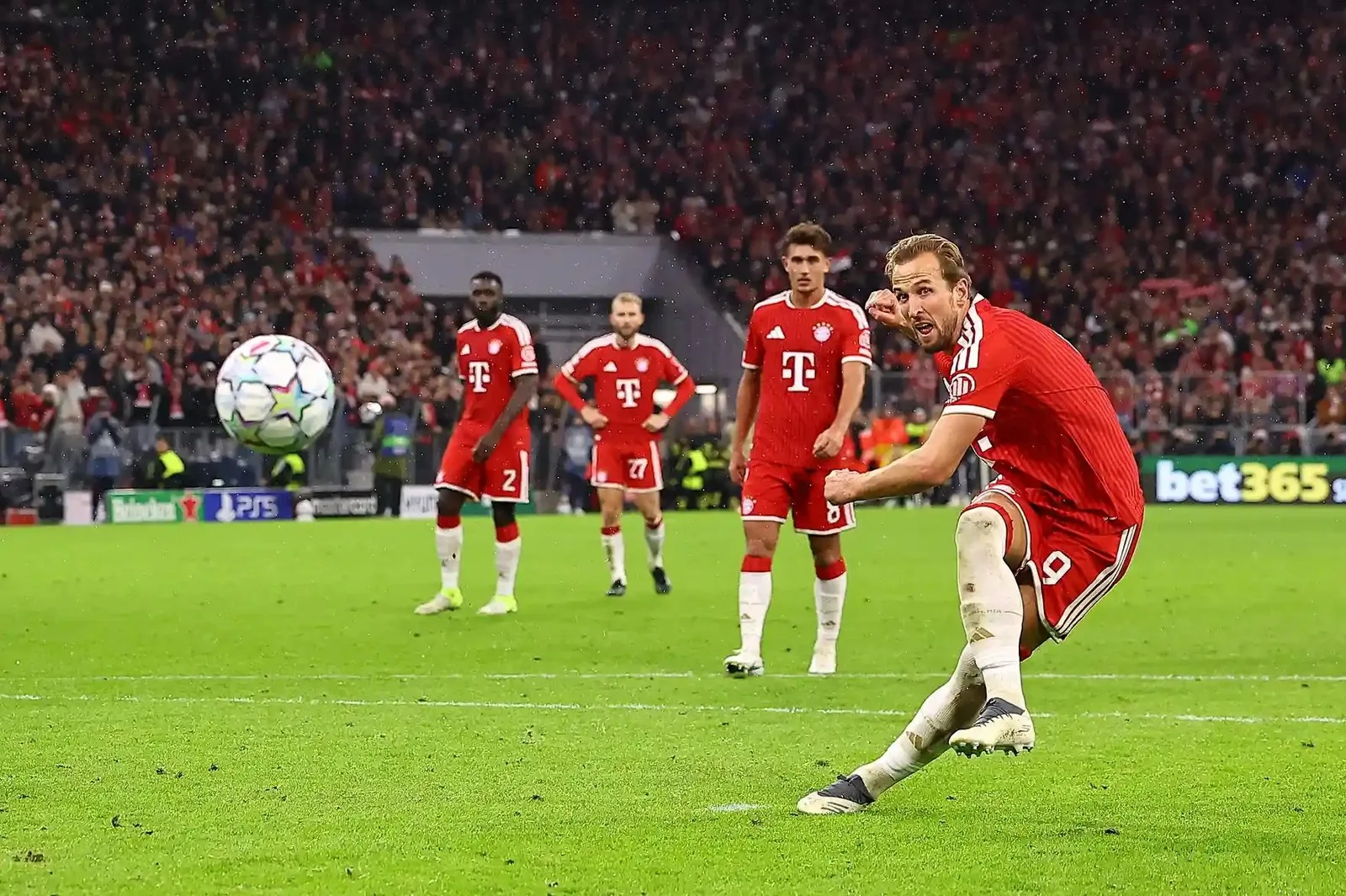 Harry Kane strikes a penalty kick for Bayern Munich as teammates watch nearby